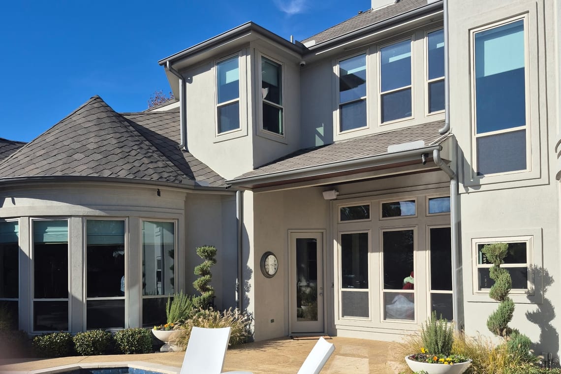 A two-storey stucco home with tall windows and glass doors beside a pool