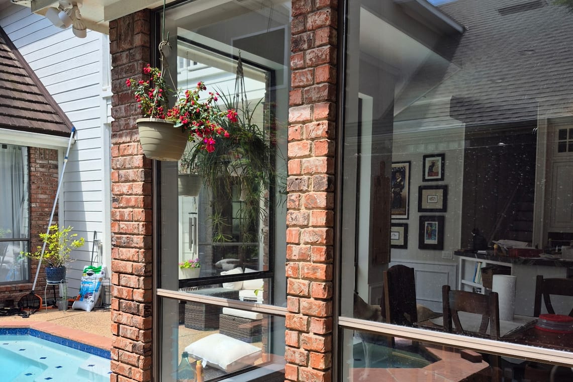 A brick sunroom wall of large glass panes beside a pool, a hanging basket in flower