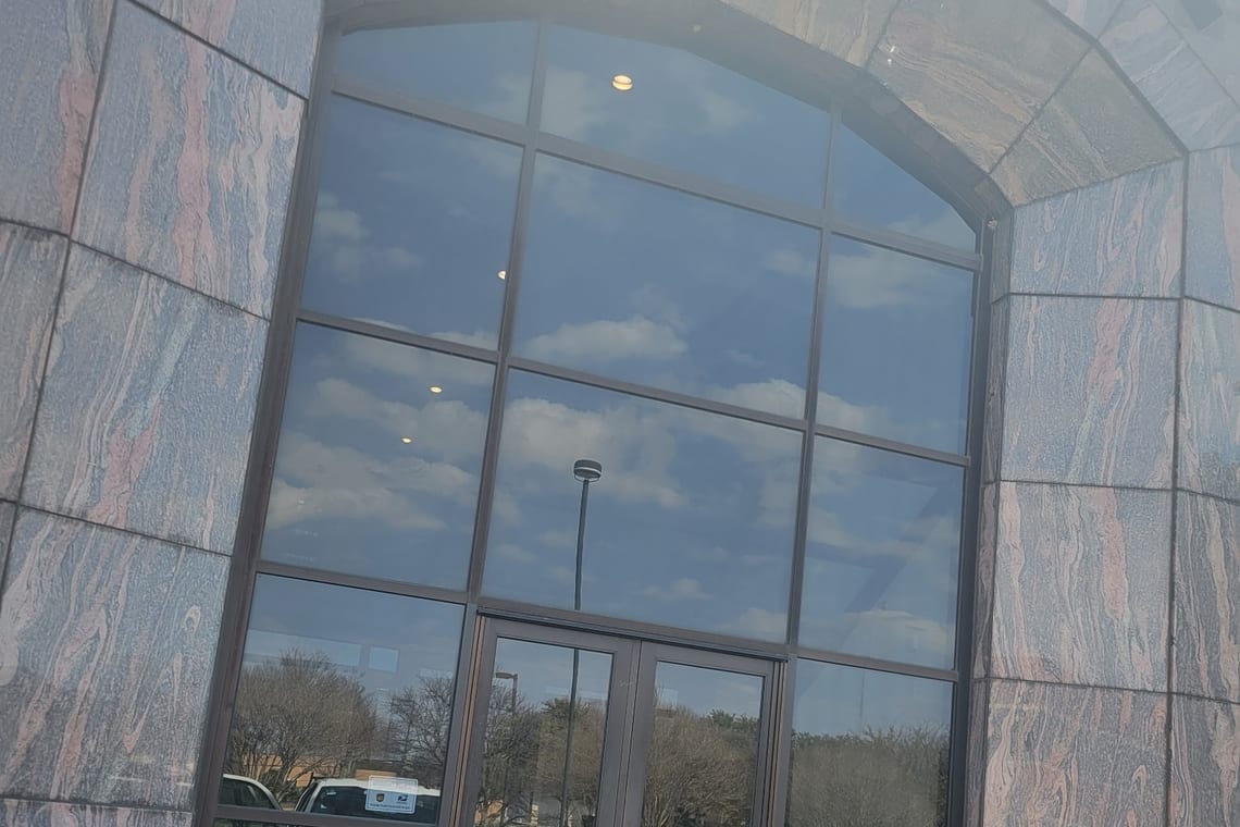 A tall arched glass entrance on a stone-clad commercial building, reflecting cloud