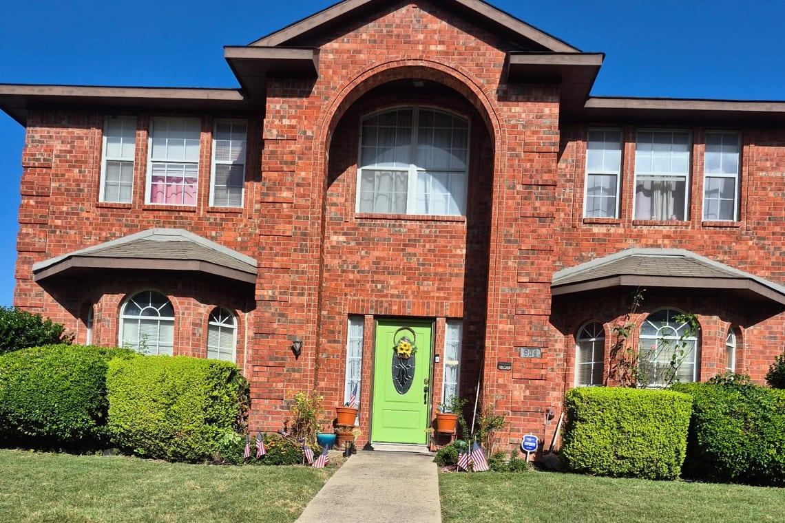 The front of a red-brick two-storey home with arched windows and a green door